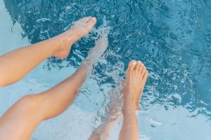 people kicking their feet in a clear blue swimming pool
