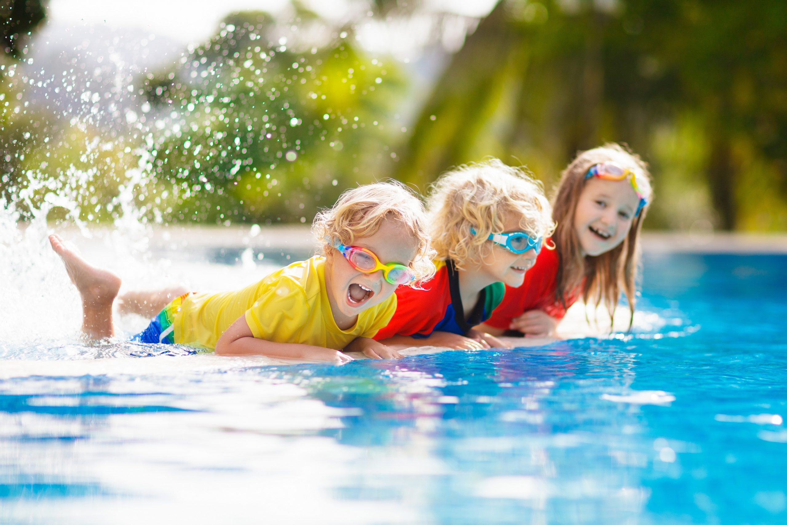 Three kids playing in blue backyard swimming pool